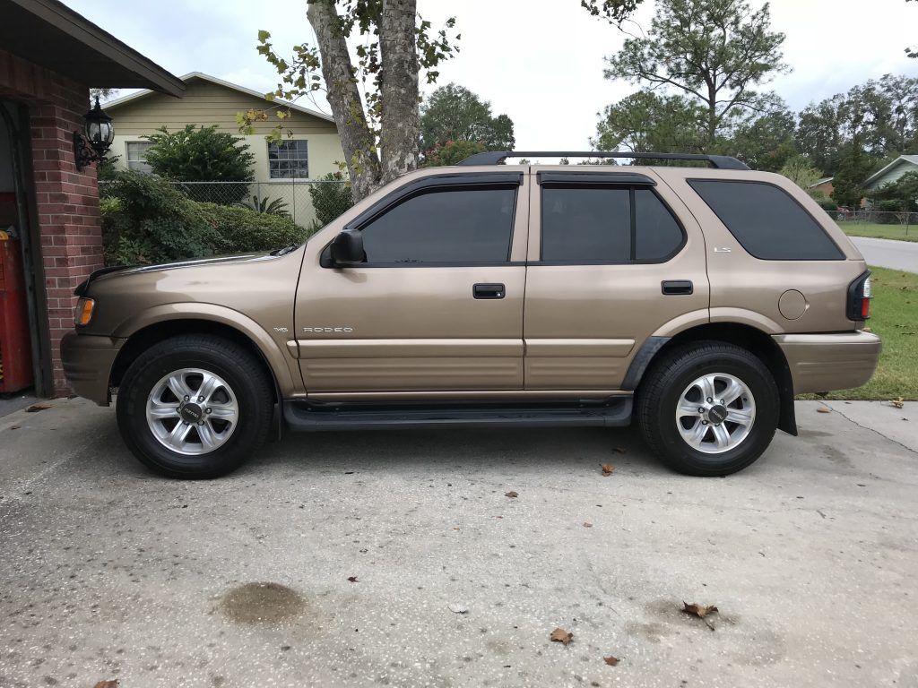 A brown suv is parked in a driveway in front of a house.