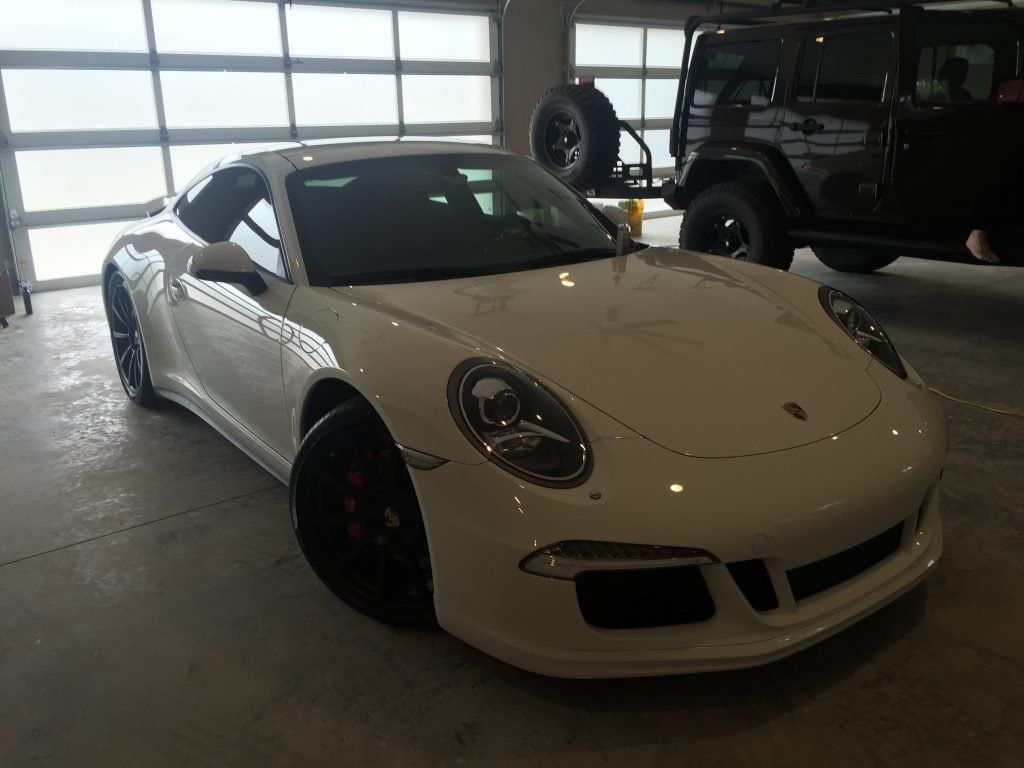 A white porsche 911 is parked in a garage next to a black jeep.