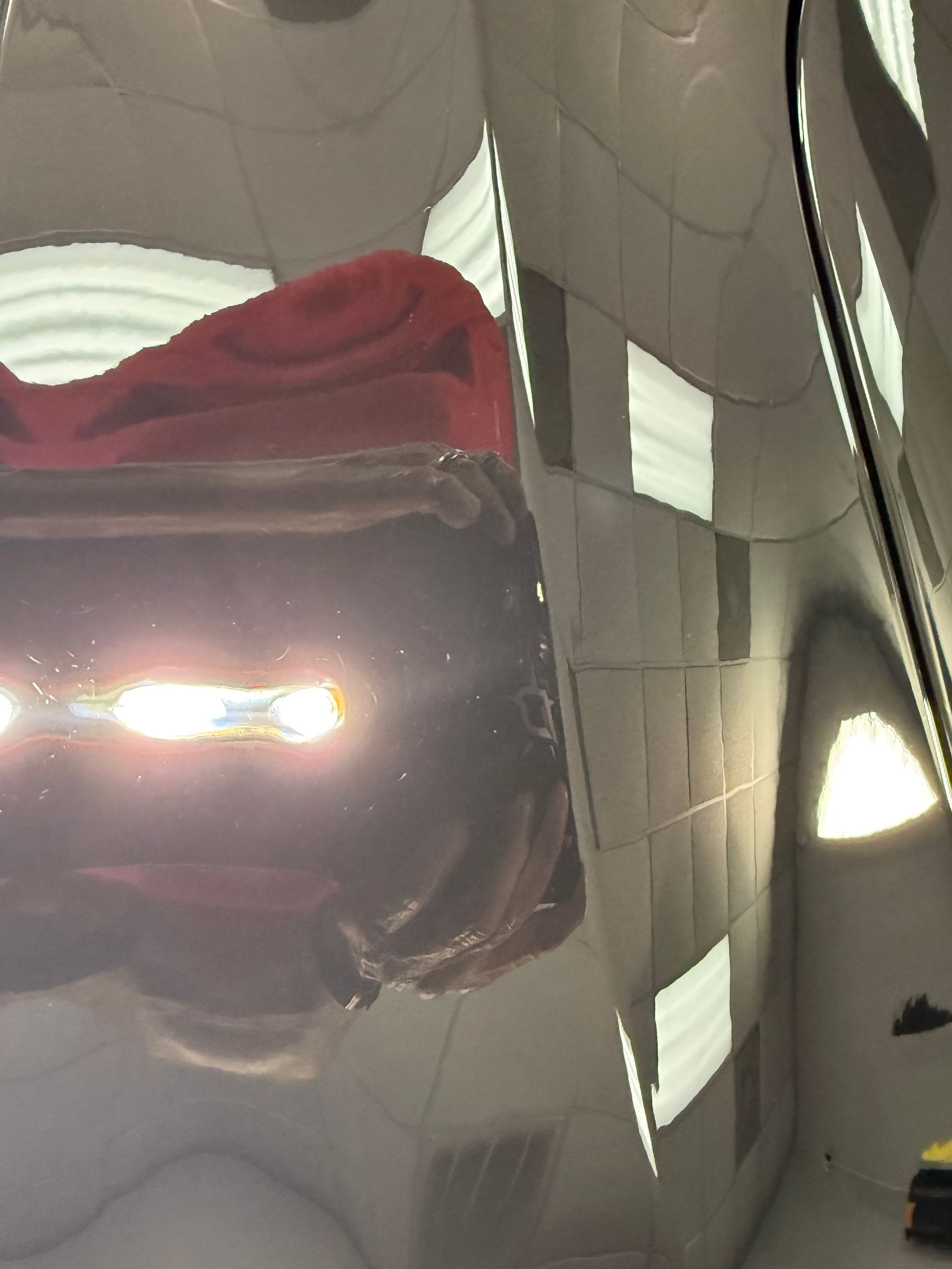 Red car’s shiny hood reflecting ceiling lights and nearby objects in a garage.