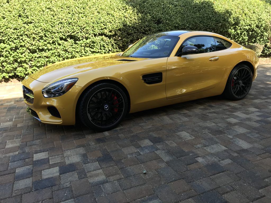 A yellow sports car is parked on a brick driveway.