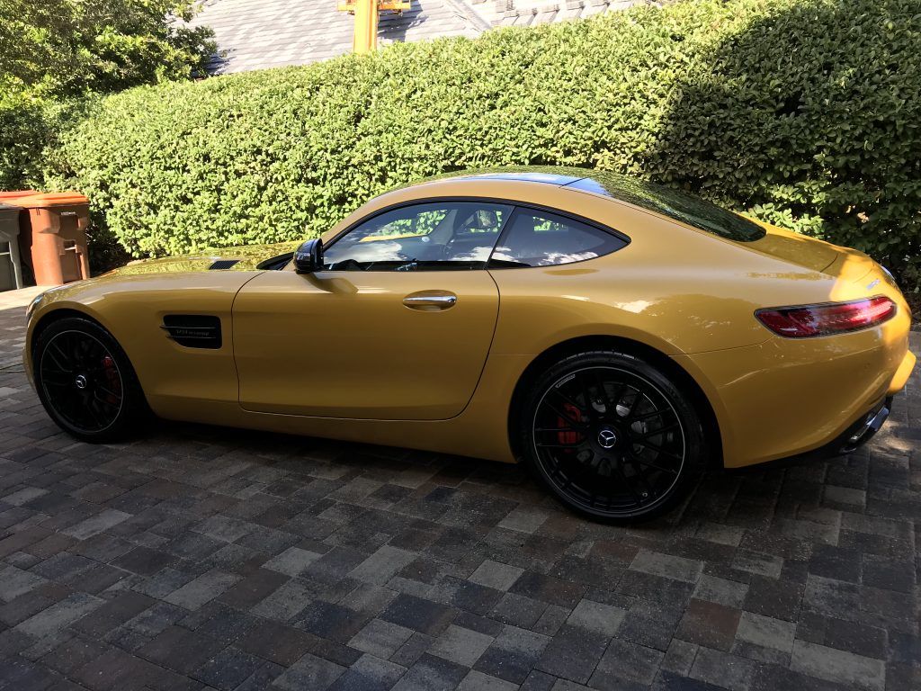 A yellow sports car is parked on a brick driveway.
