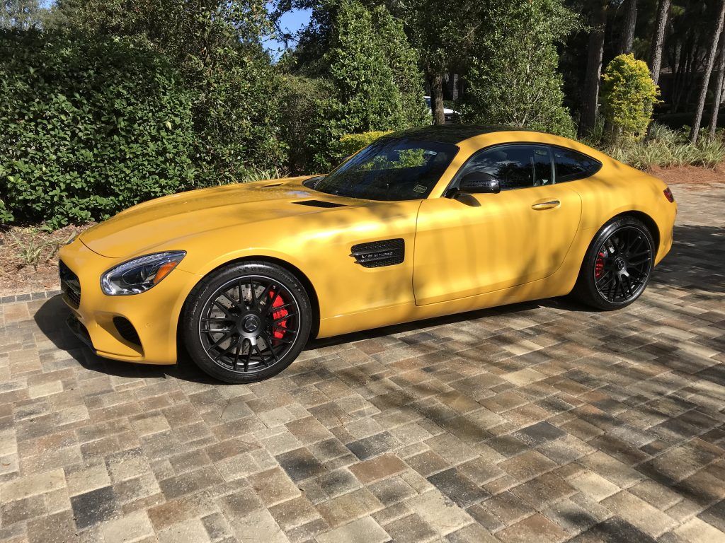 A yellow mercedes benz amg gt is parked on a brick driveway.