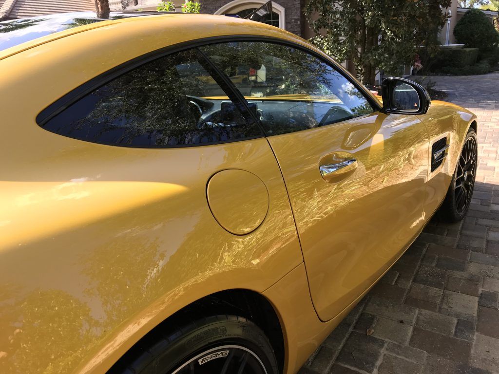 A yellow sports car is parked on a brick driveway.