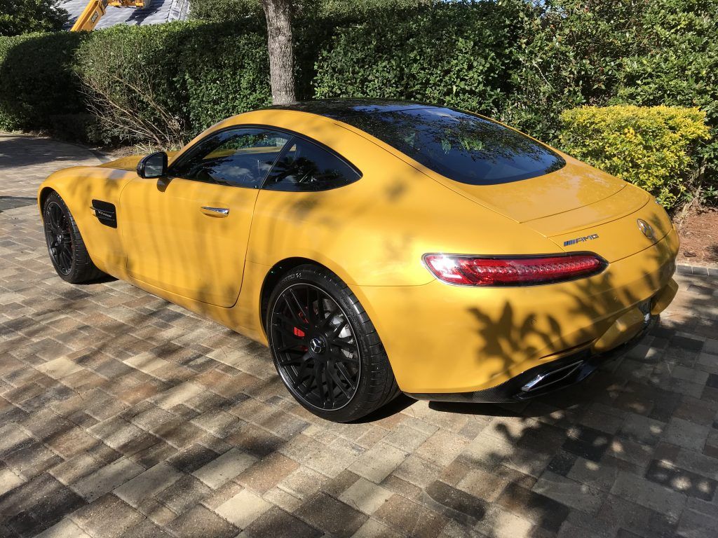A yellow sports car is parked on a brick driveway.