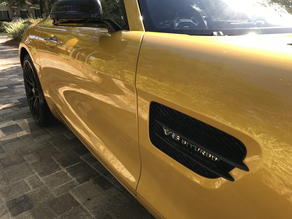 A yellow sports car is parked on a brick driveway.