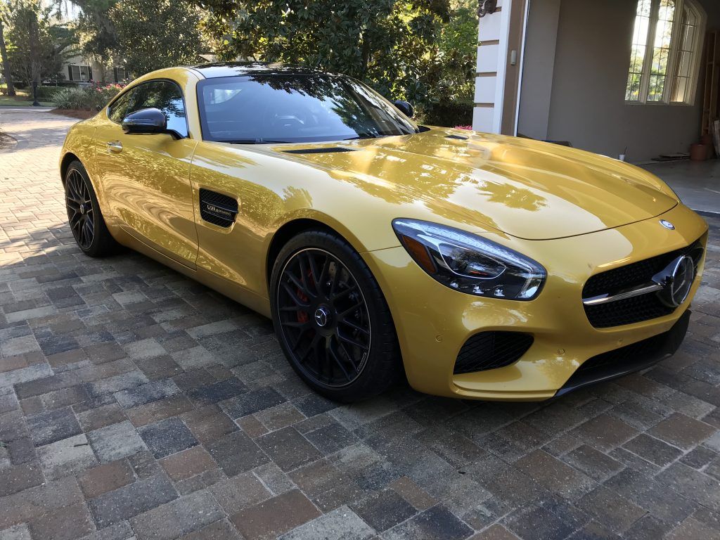 A yellow mercedes benz amg gt is parked in a driveway.