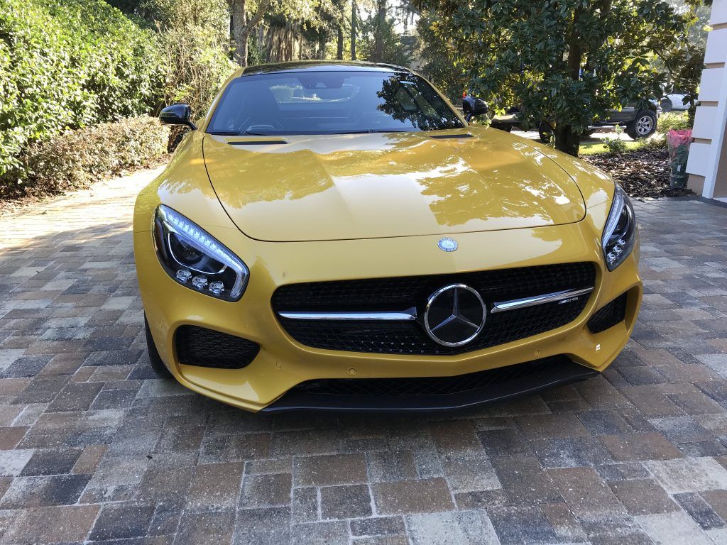 A yellow mercedes benz is parked on a brick driveway.