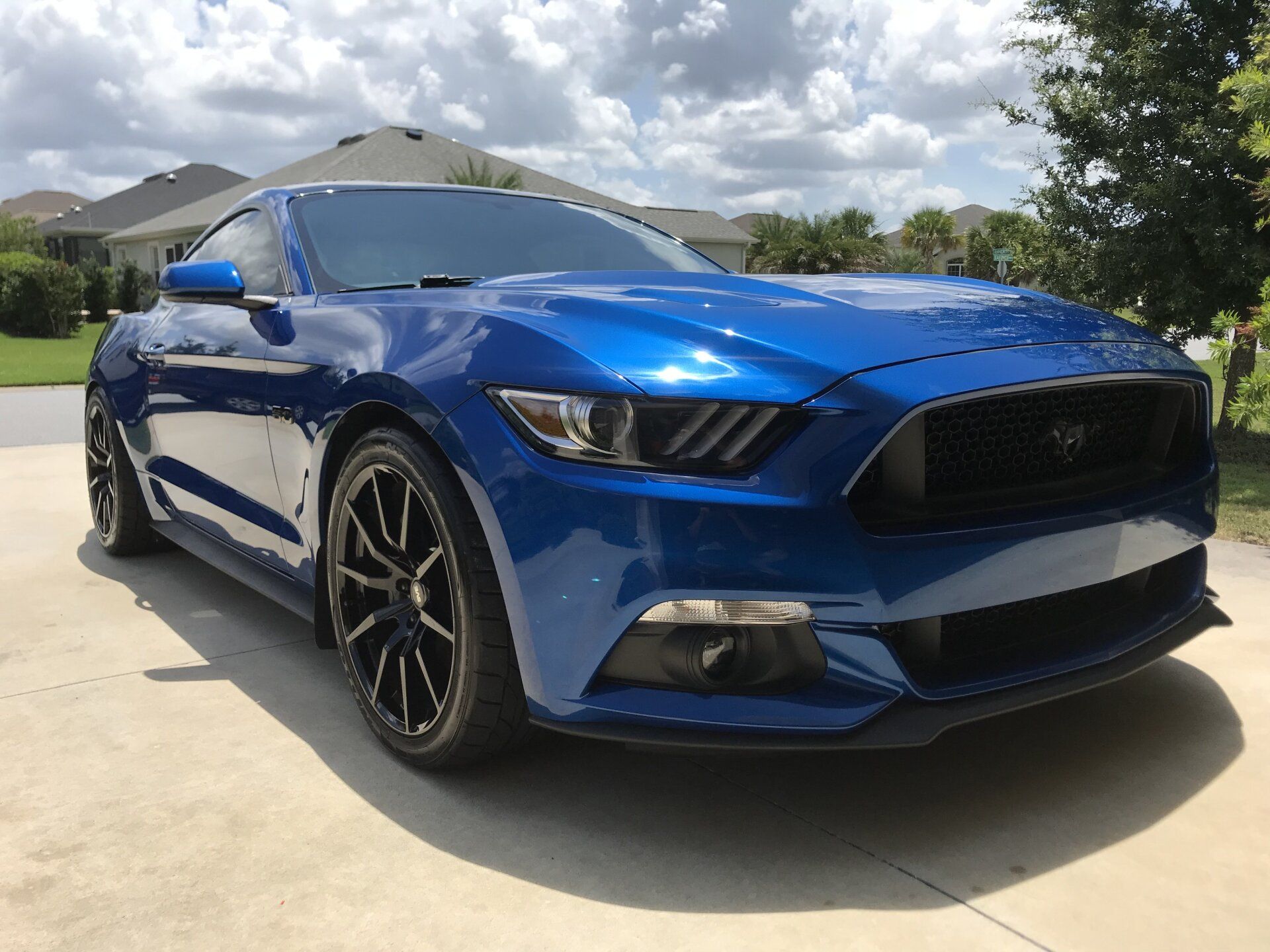 A blue mustang is parked in a driveway in front of a house.