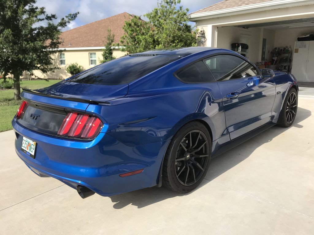 A blue mustang is parked in a driveway in front of a house.