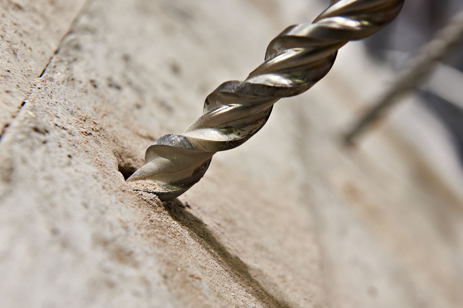 Close-up of a drill bit boring into a dusty wooden surface.