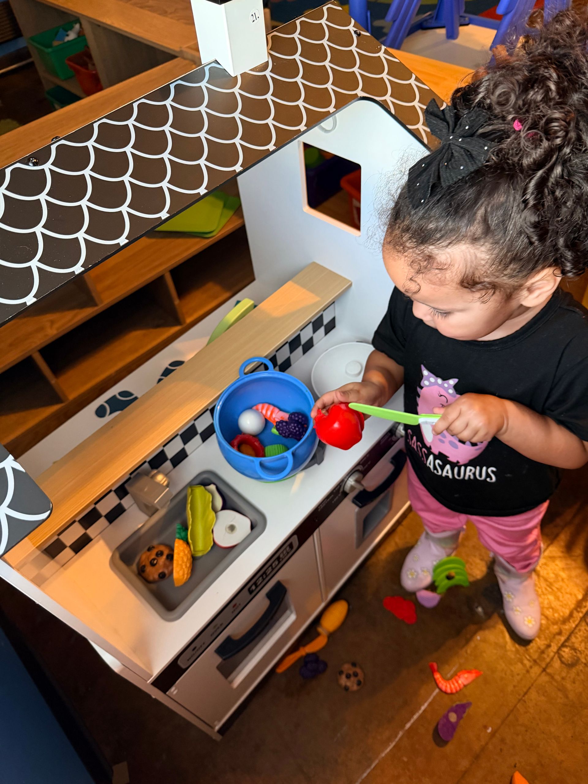 A child playing with toy kitchen appliances, holding a toy tomato.