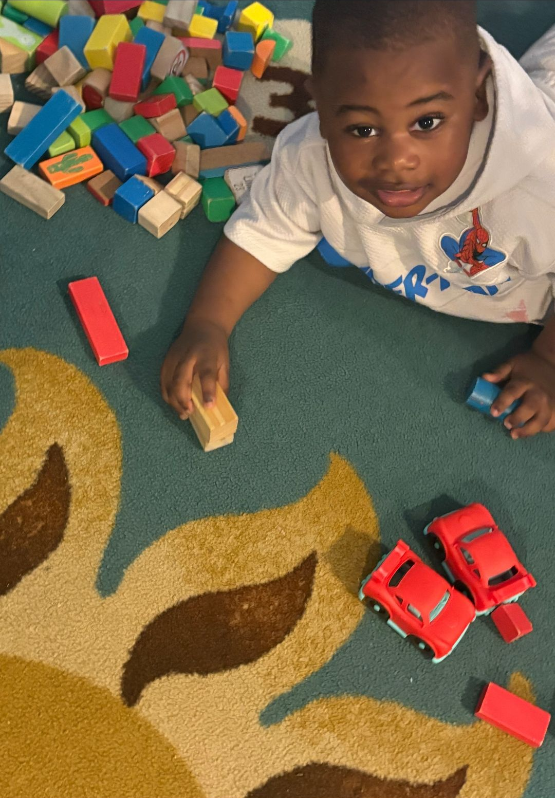 Boy playing with blocks and toy cars on a colorful rug.
