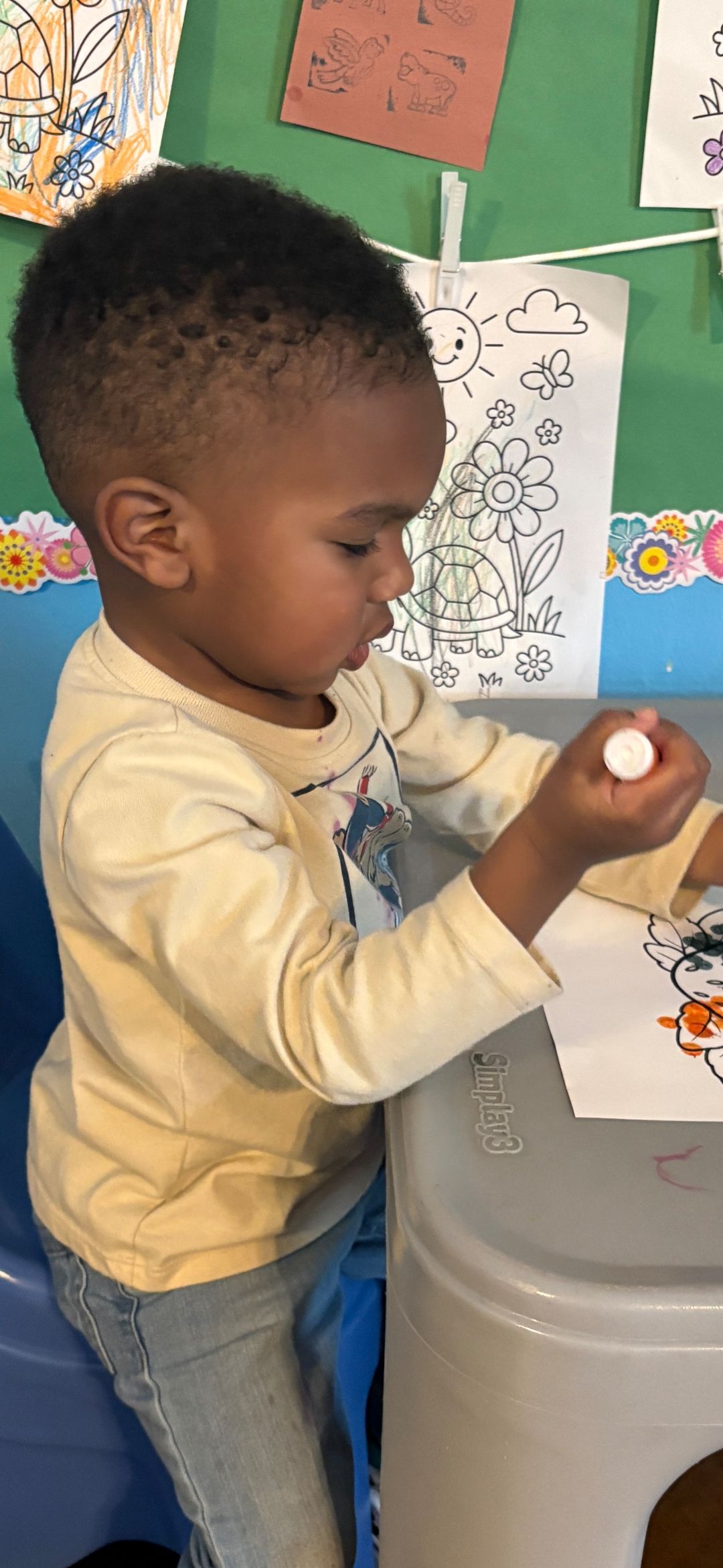 A child at a table holds a glue stick, focused on coloring.