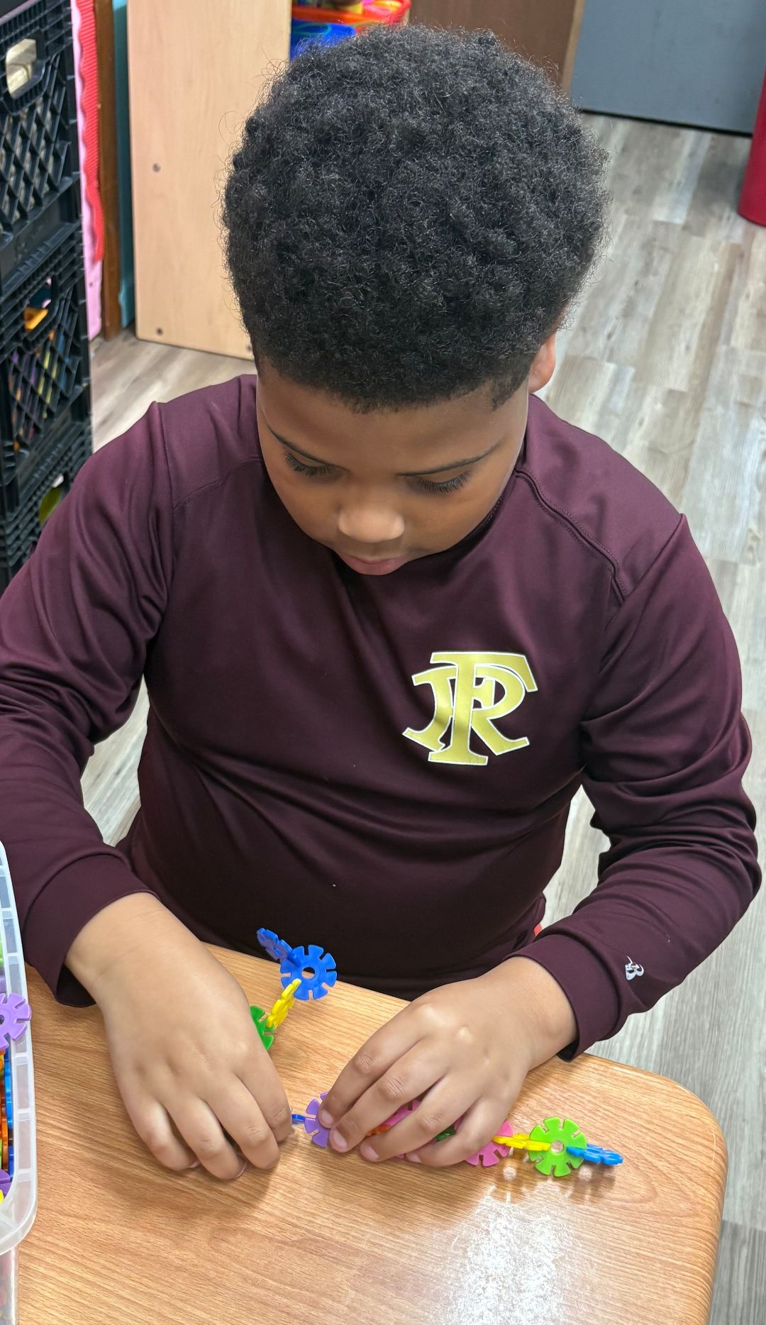 Boy in maroon shirt building with colorful blocks at a table.