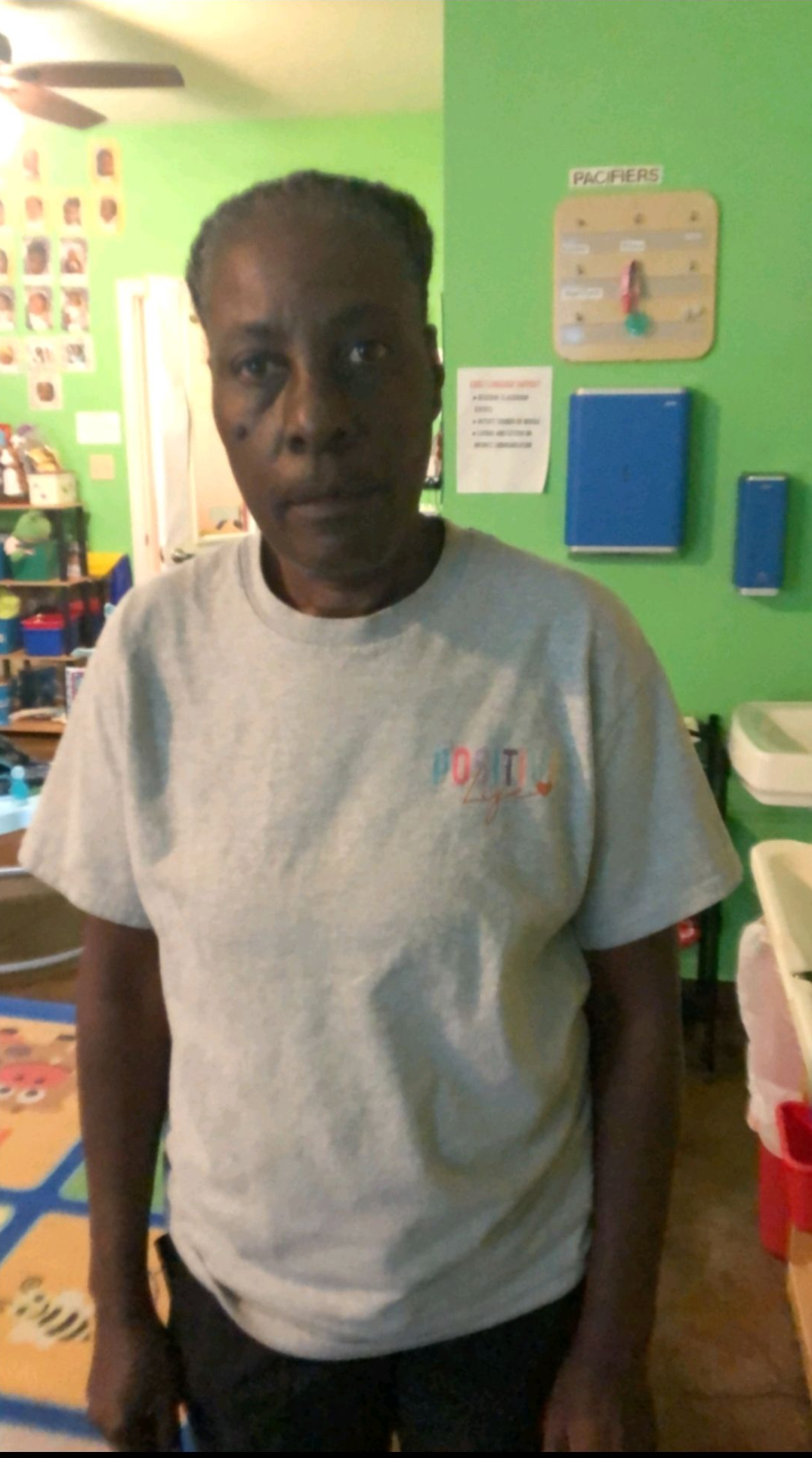 Woman wearing a gray t-shirt stands in a room with green walls.