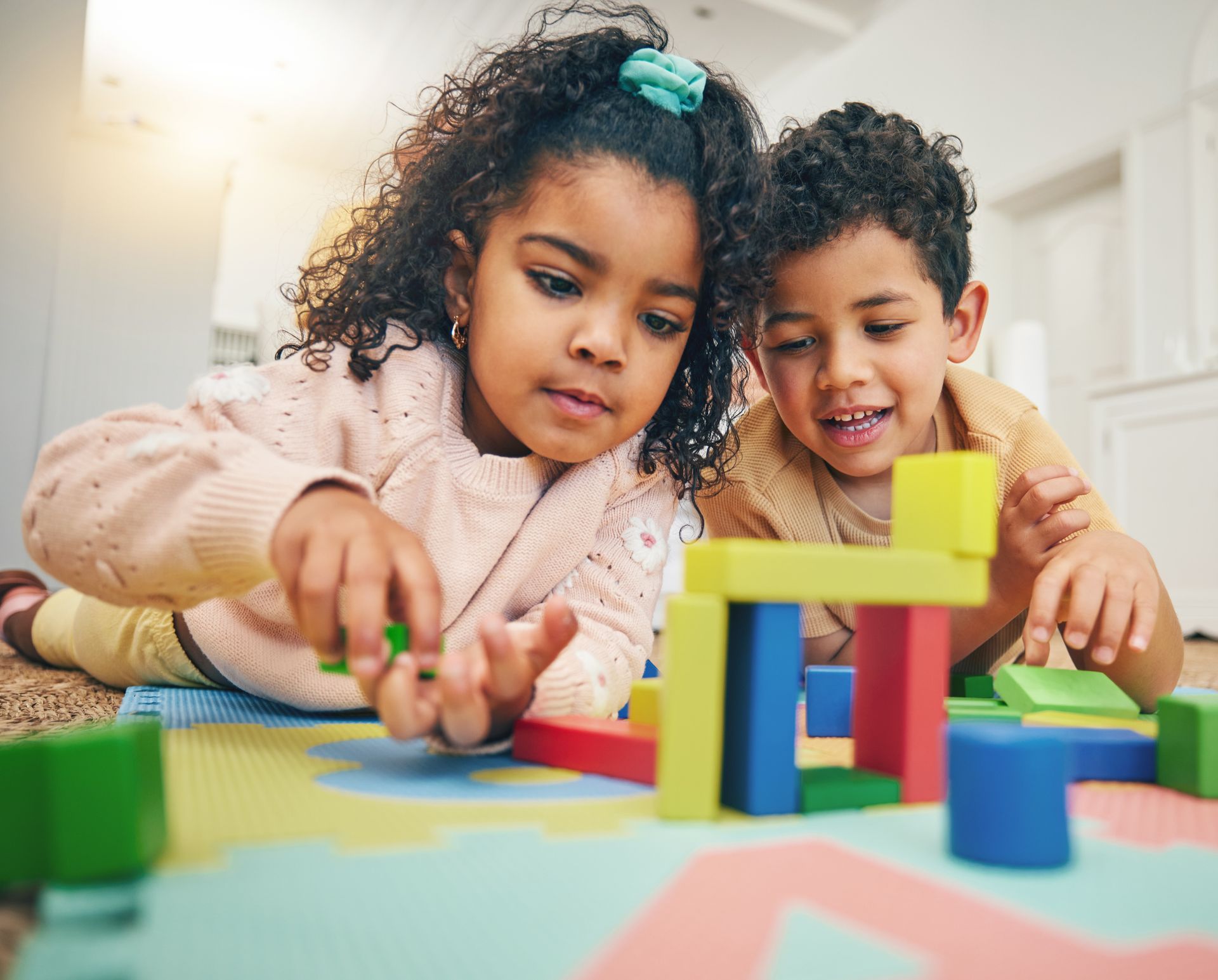 Two children playing with colorful wooden blocks on a mat.