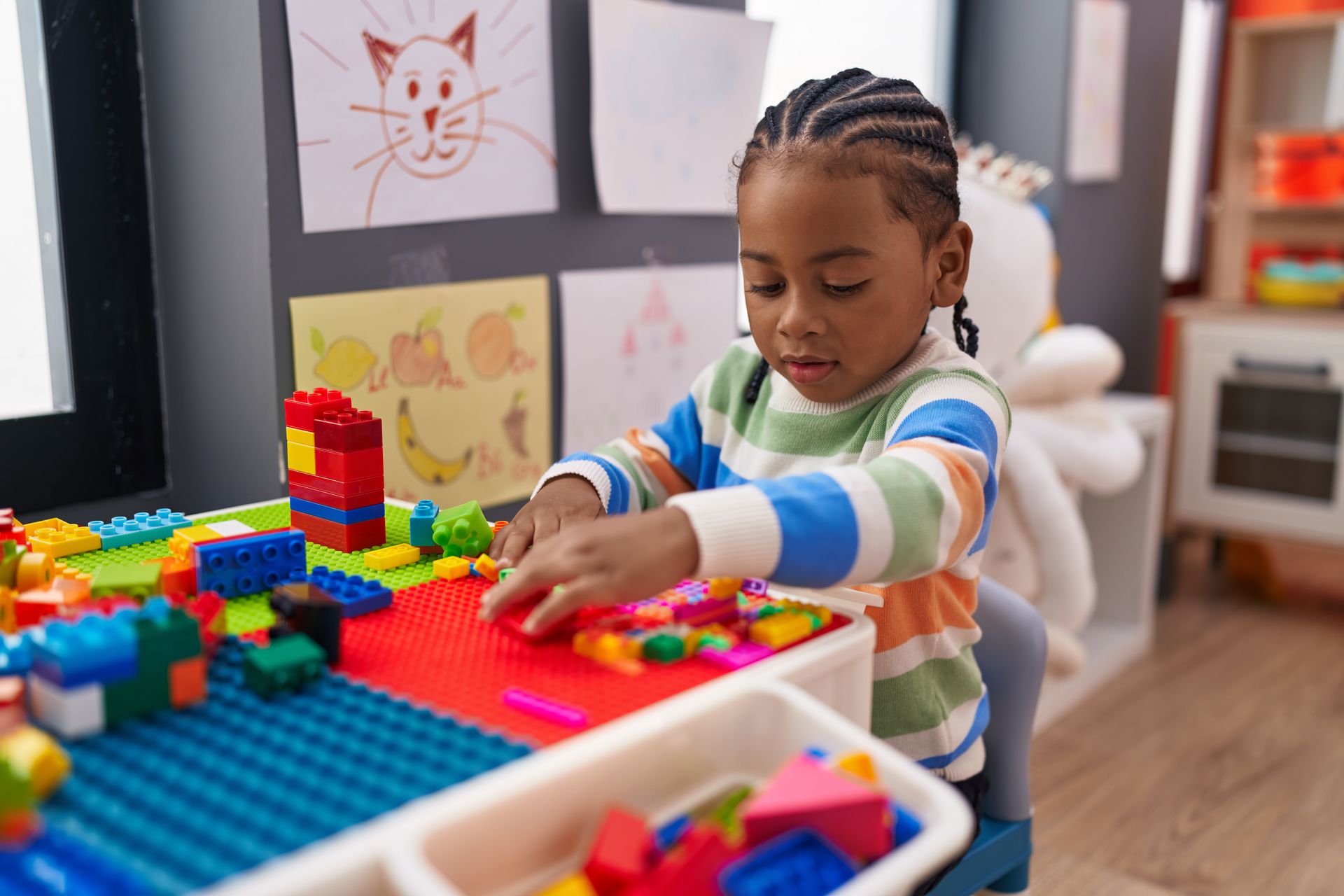 Child playing with colorful building blocks at a table in a classroom.