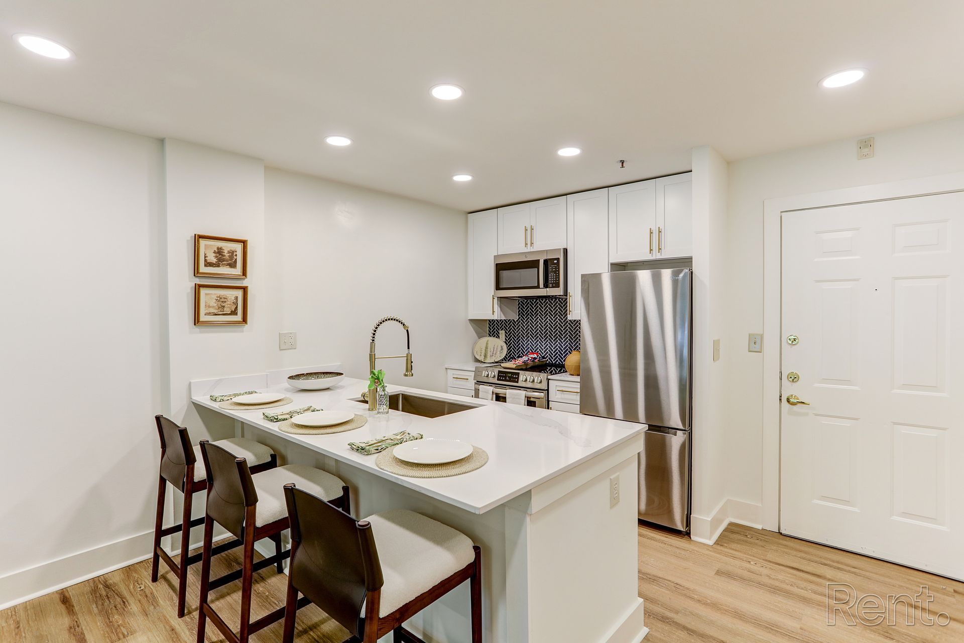 Modern kitchen with white cabinets, stainless steel appliances, and a breakfast bar with three stools.