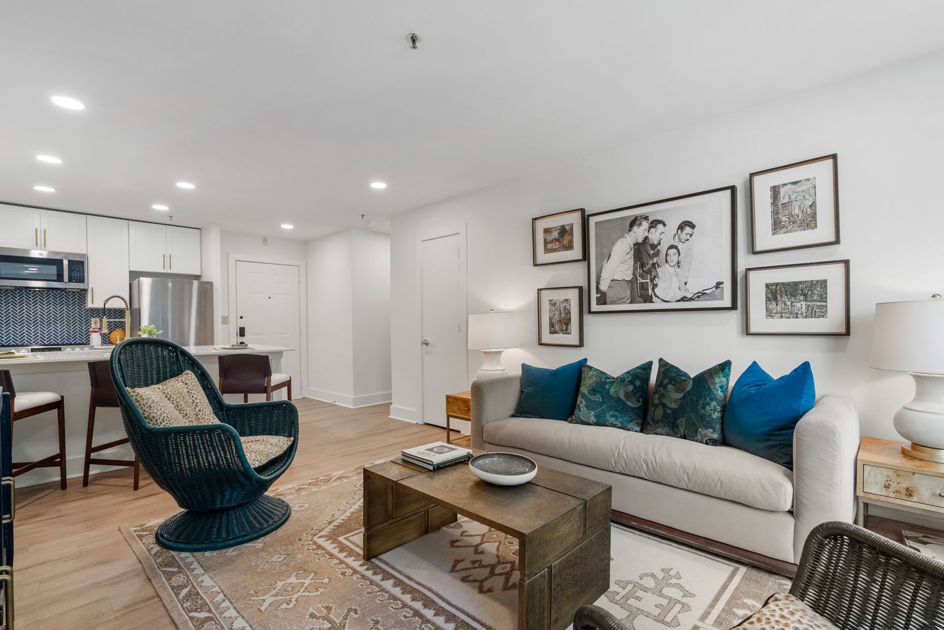 Living room with light-colored sofa, framed photos on the wall, and kitchen in the background.