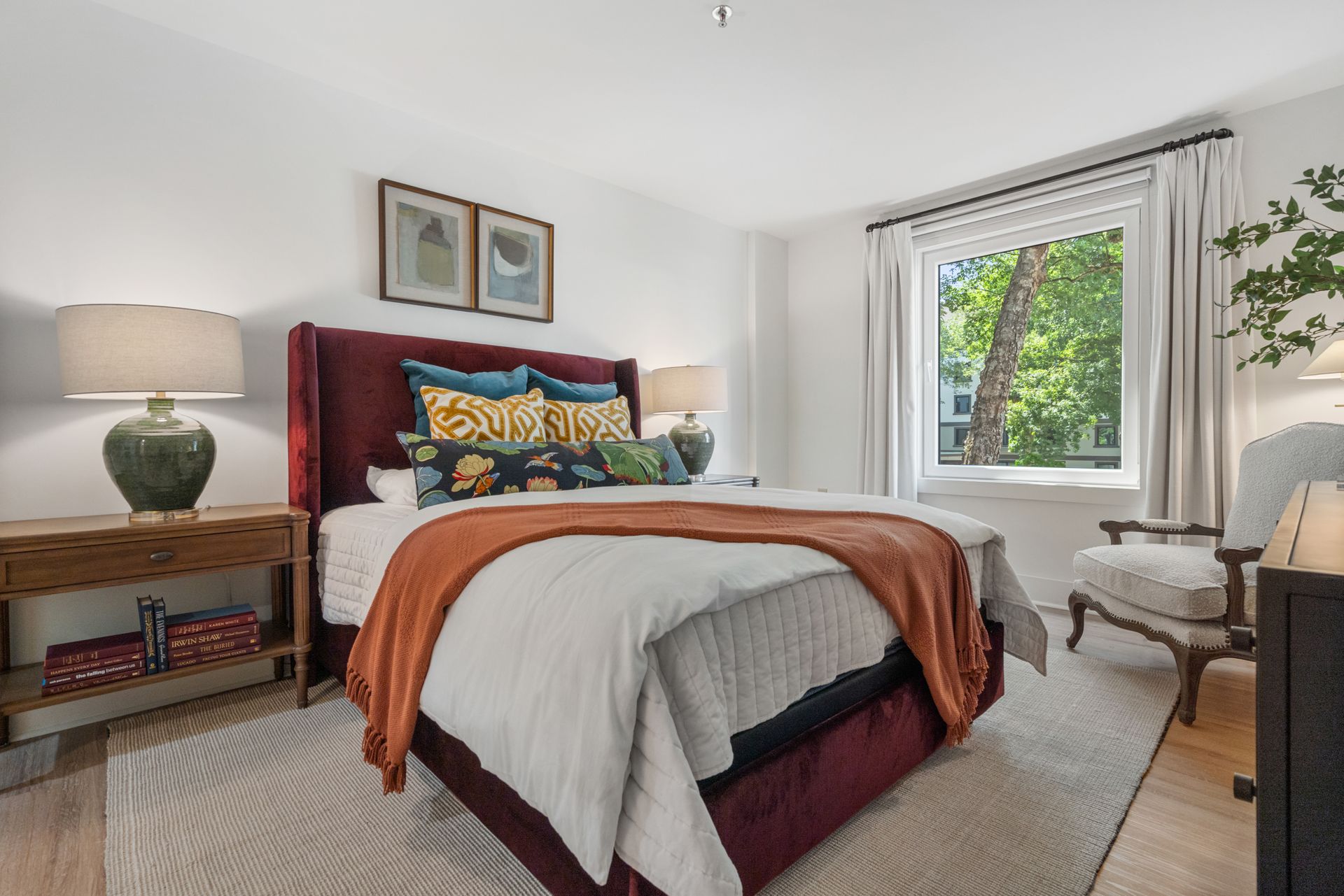 Bedroom with red upholstered bed, nightstands, and window with greenery view.