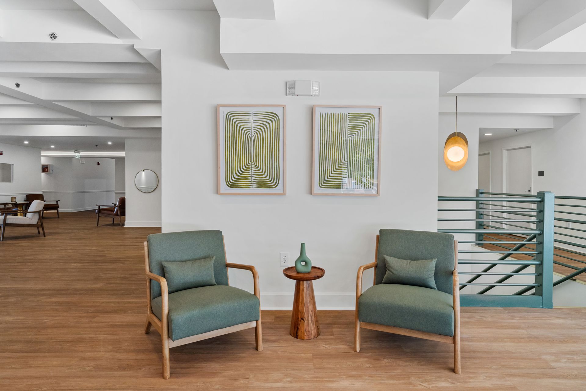 Two comfortable chairs and a decorative table below colorful paintings in the lobby at Clairmont Crest senior living apartments in Decatur, GA.
