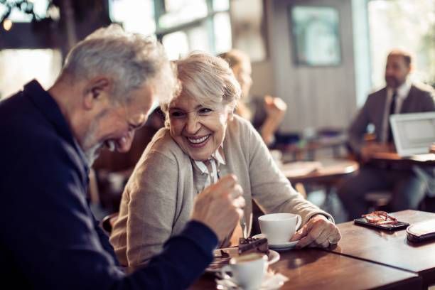 An elderly couple is sitting at a table in a restaurant drinking coffee.