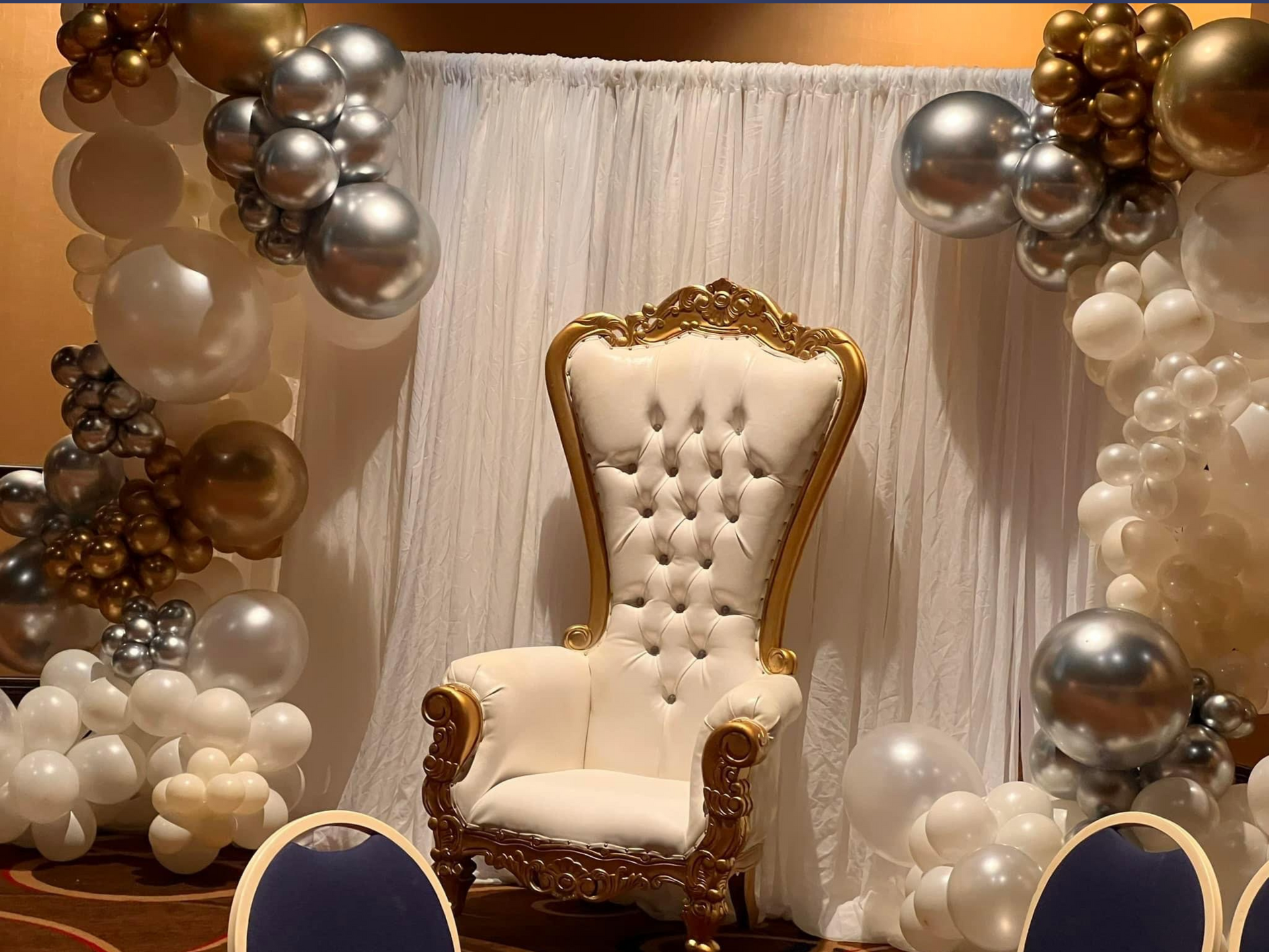 A white chair is sitting in front of a wall of balloons.