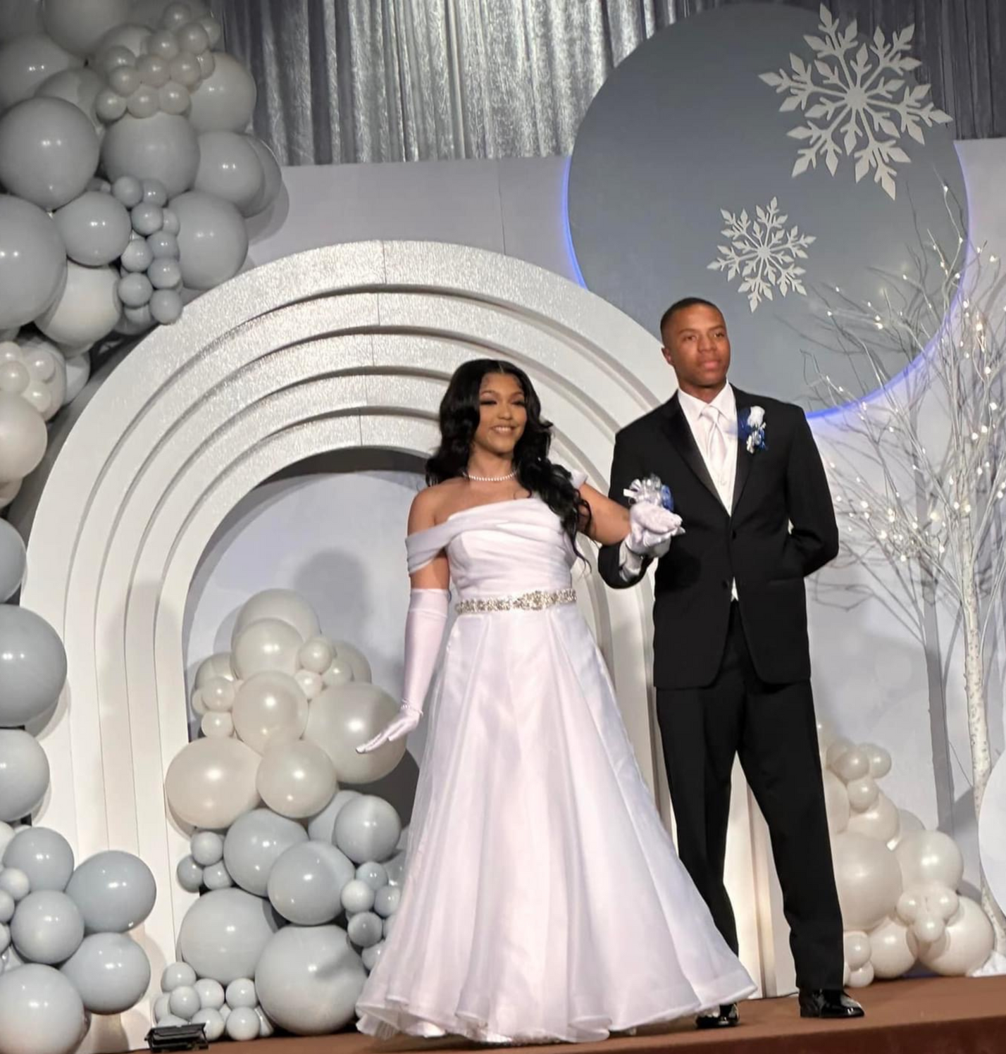 A bride and groom stand on a stage with balloons in the background