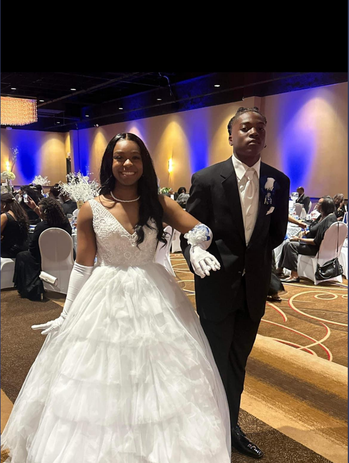 A woman in a white dress and a man in a suit are standing next to each other in a ballroom.