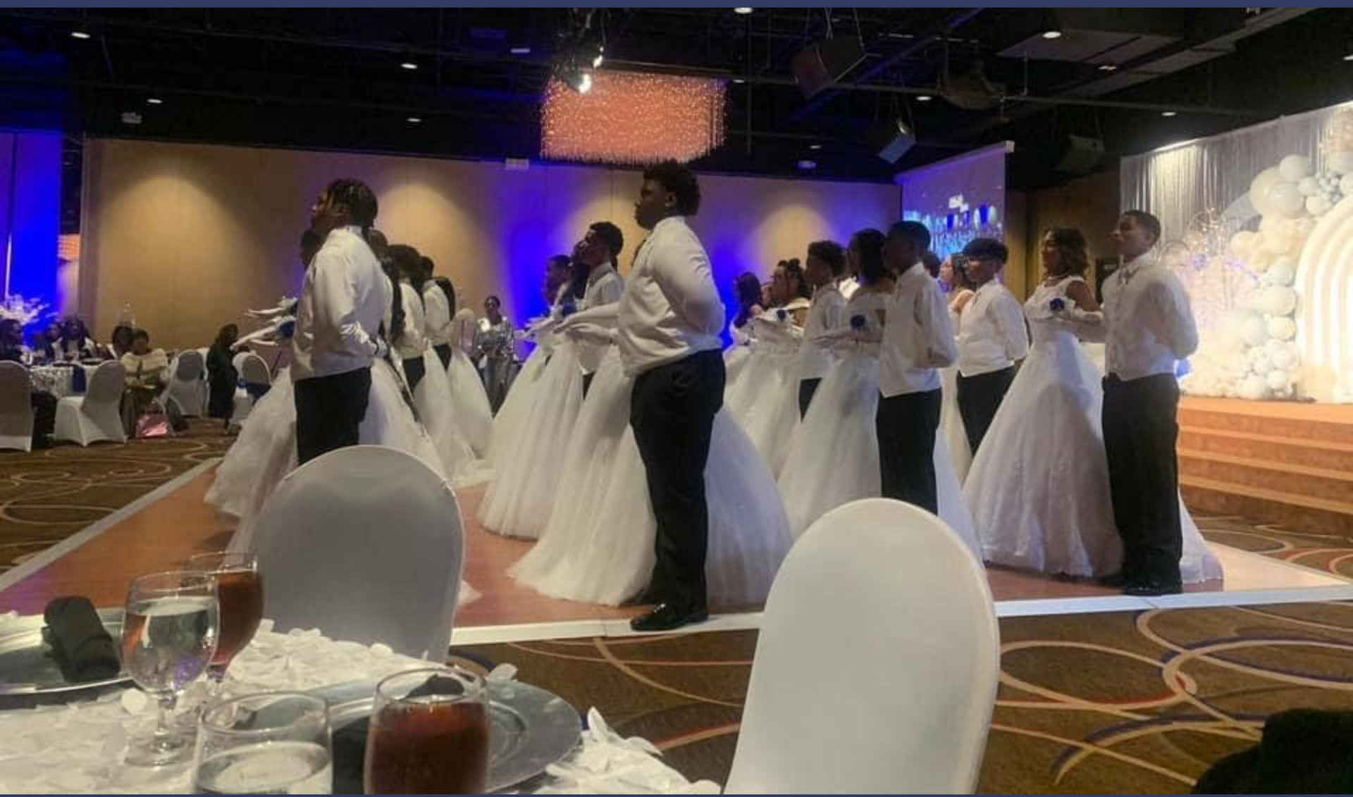A group of people in white dresses are dancing in a ballroom.