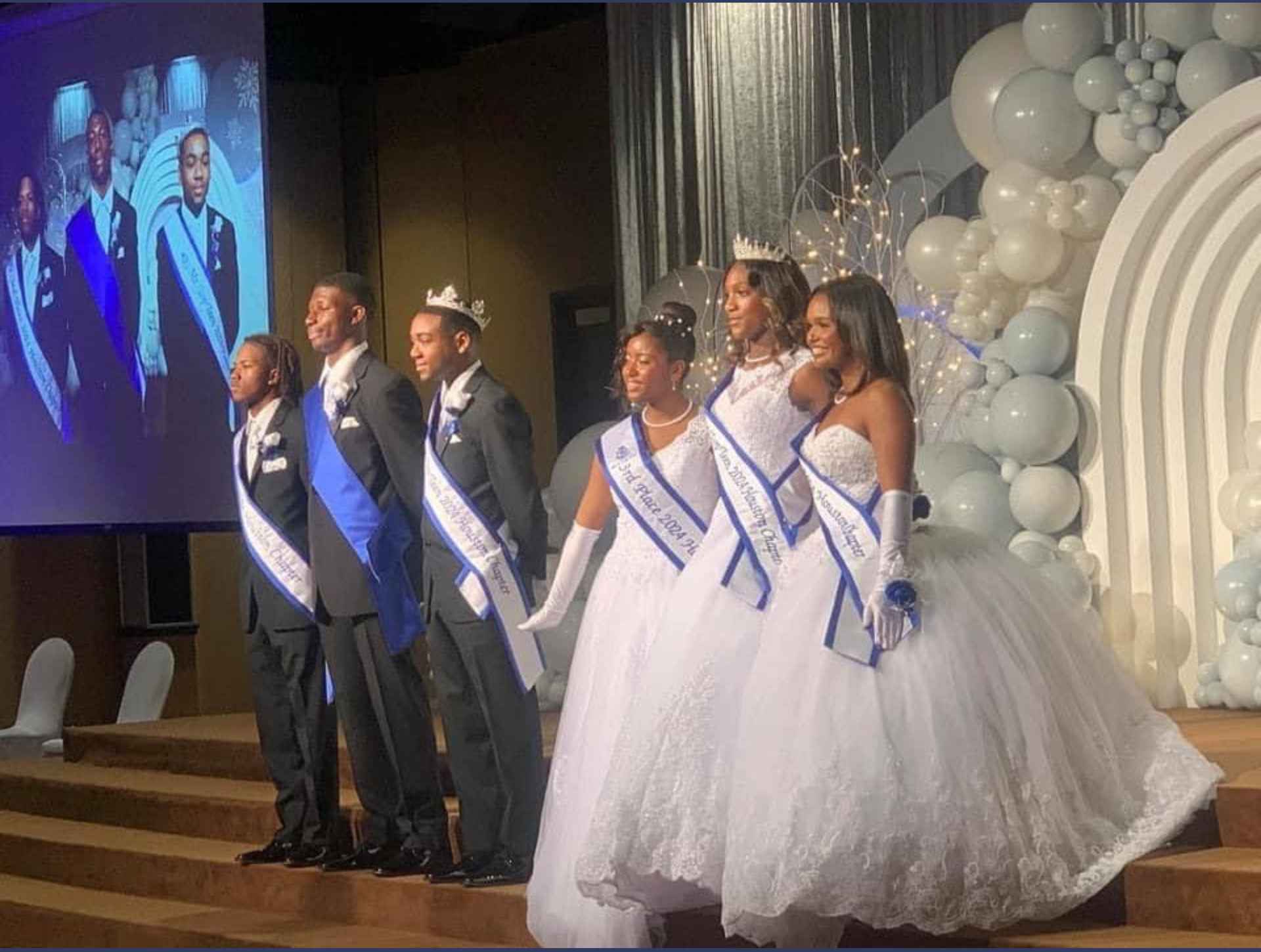 A group of people in white dresses and tuxedos are standing on a stage.