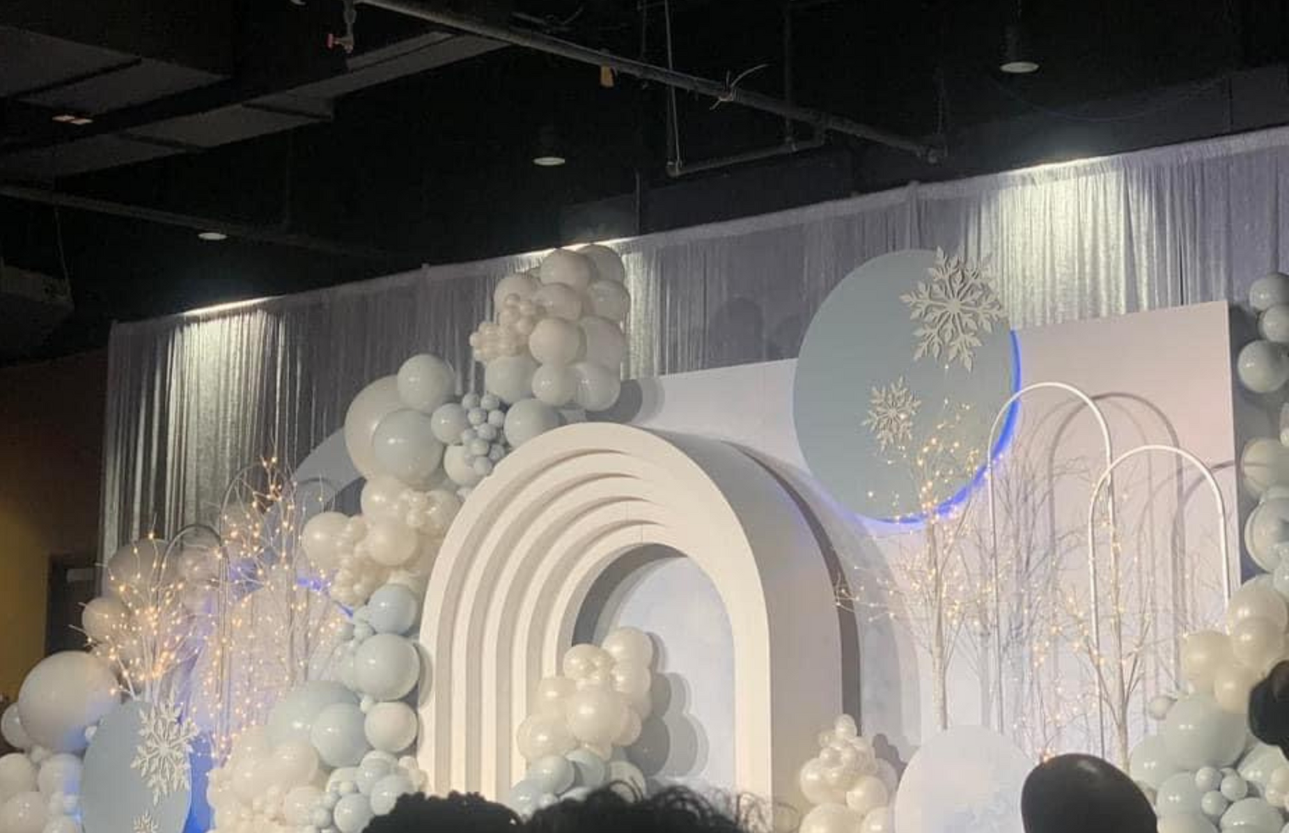 A group of people are standing in front of a stage decorated with balloons and snowflakes.
