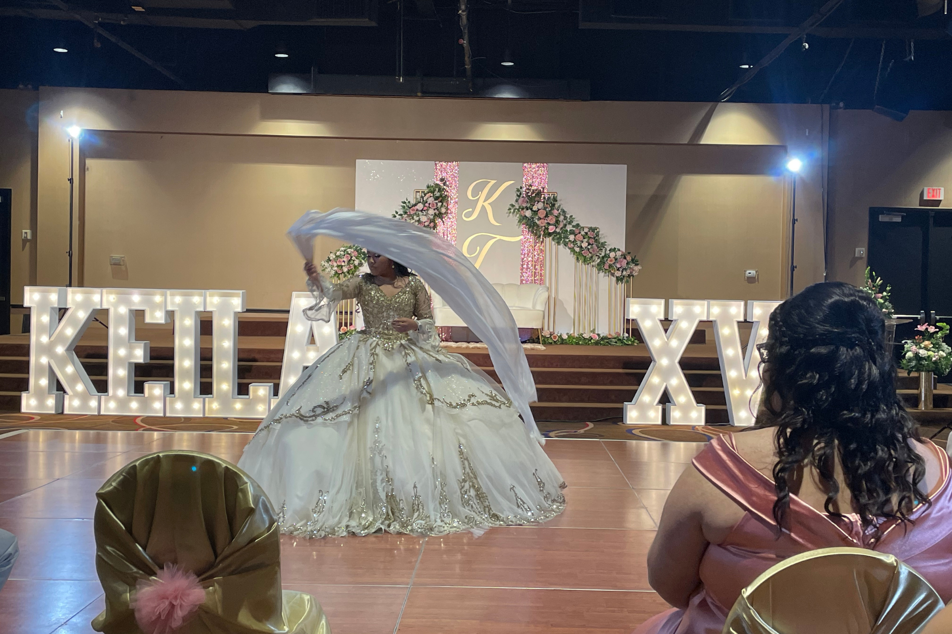 A woman in a ball gown is dancing on a stage in front of a sign that says 