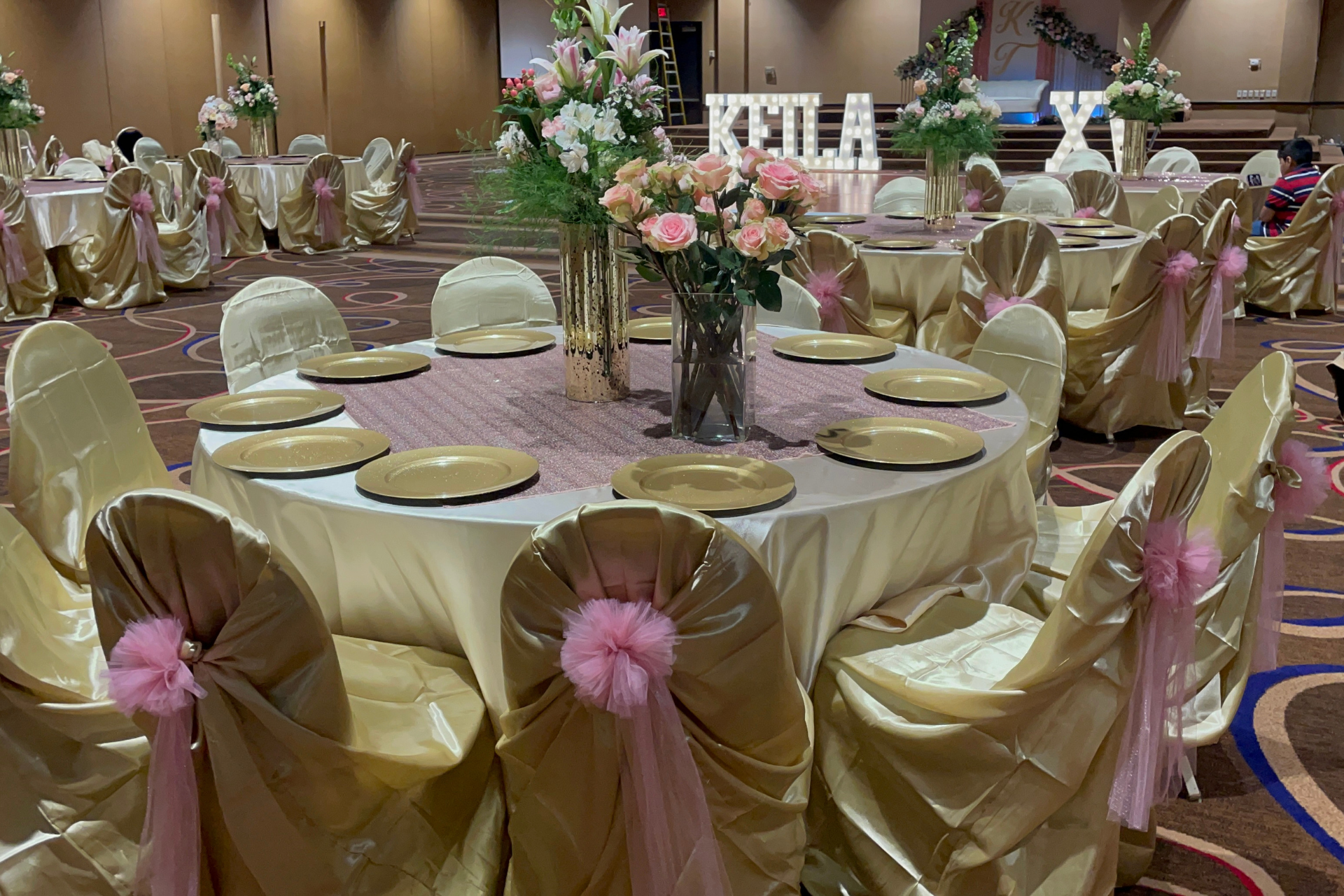 A large room with tables and chairs set up for a quinceañera event.