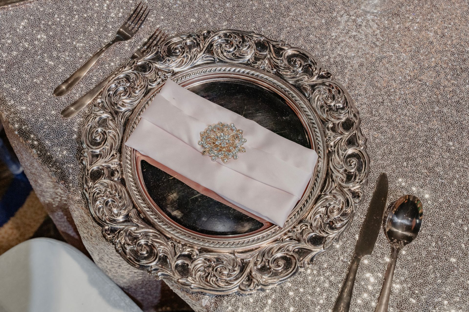 A silver plate with a napkin on it and silverware on a table.