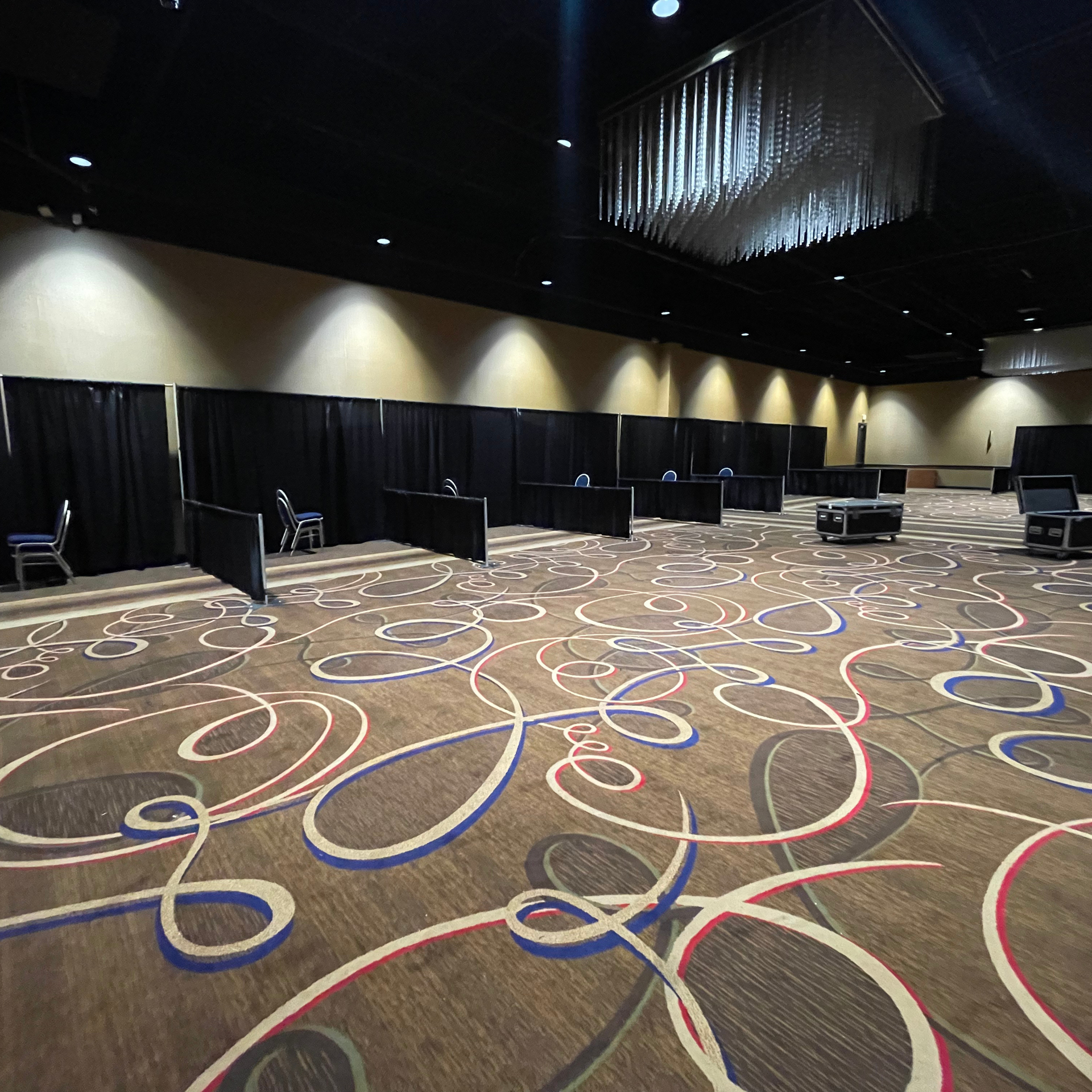 Large empty event space with patterned carpet and black dividers, tables, and chairs.