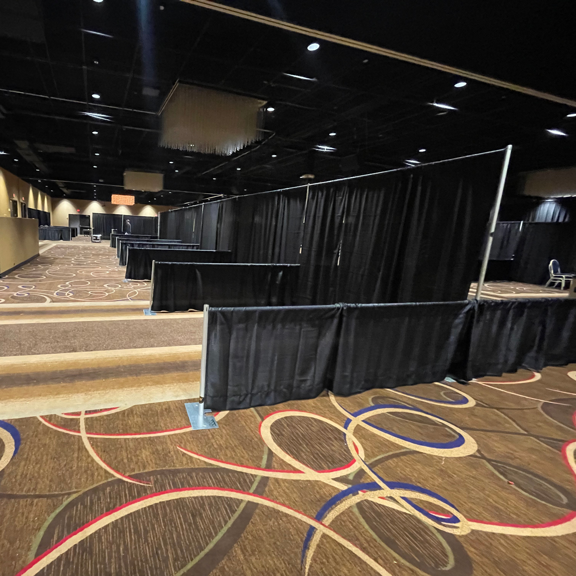 Empty convention hall with black draped booths and patterned carpet.