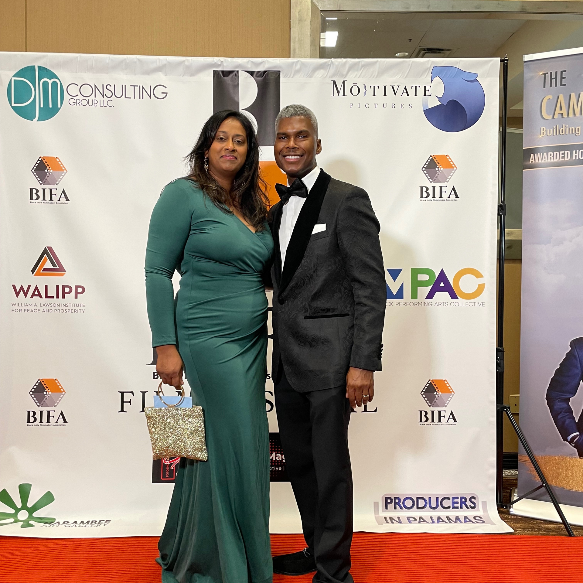 A man and a woman are posing for a picture in front of a wall that says producers
