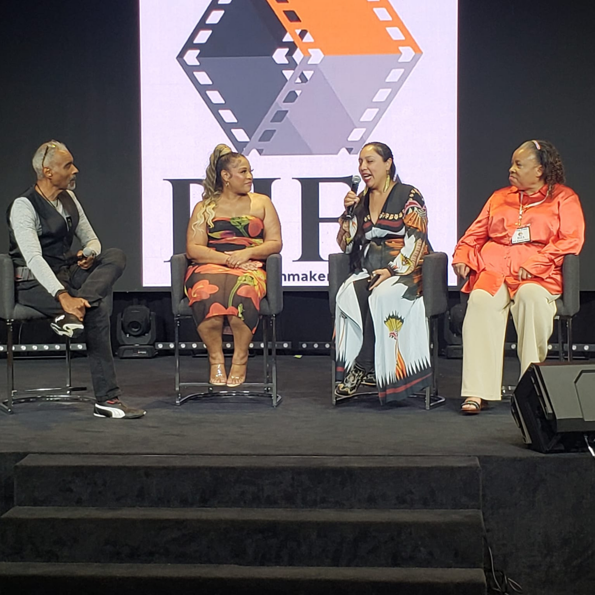 A group of people are sitting on a stage in front of a screen that says ff