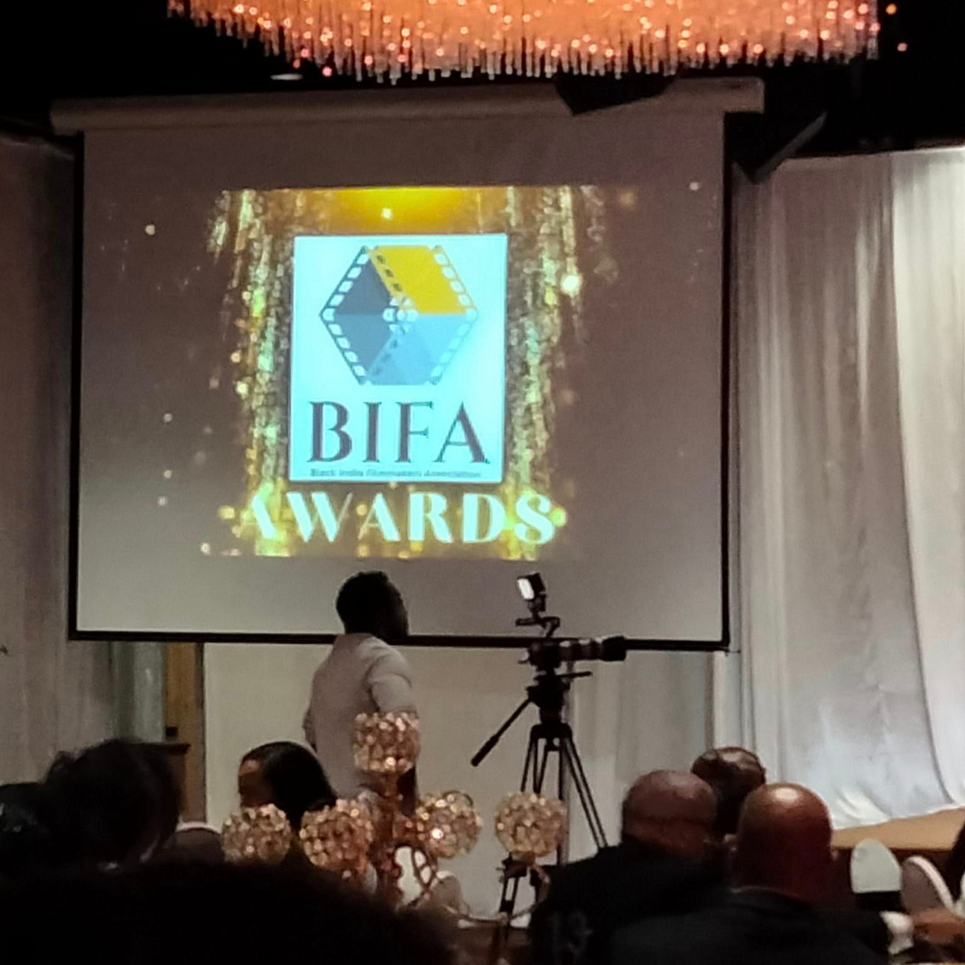 A man stands in front of a screen that says bifa awards