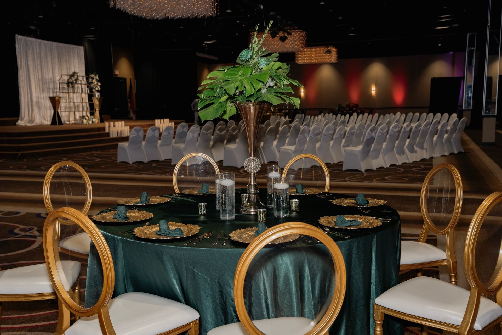 A table with a green tablecloth and gold chairs in a large room.