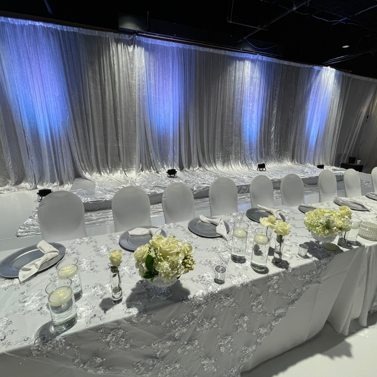 A long white table with white chairs and flowers on it.