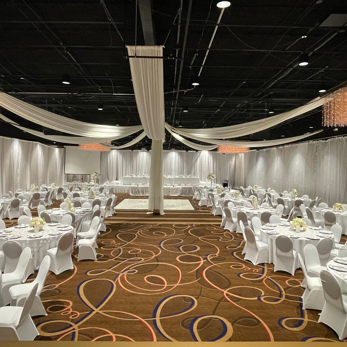 A large room with tables and chairs set up for a wedding reception