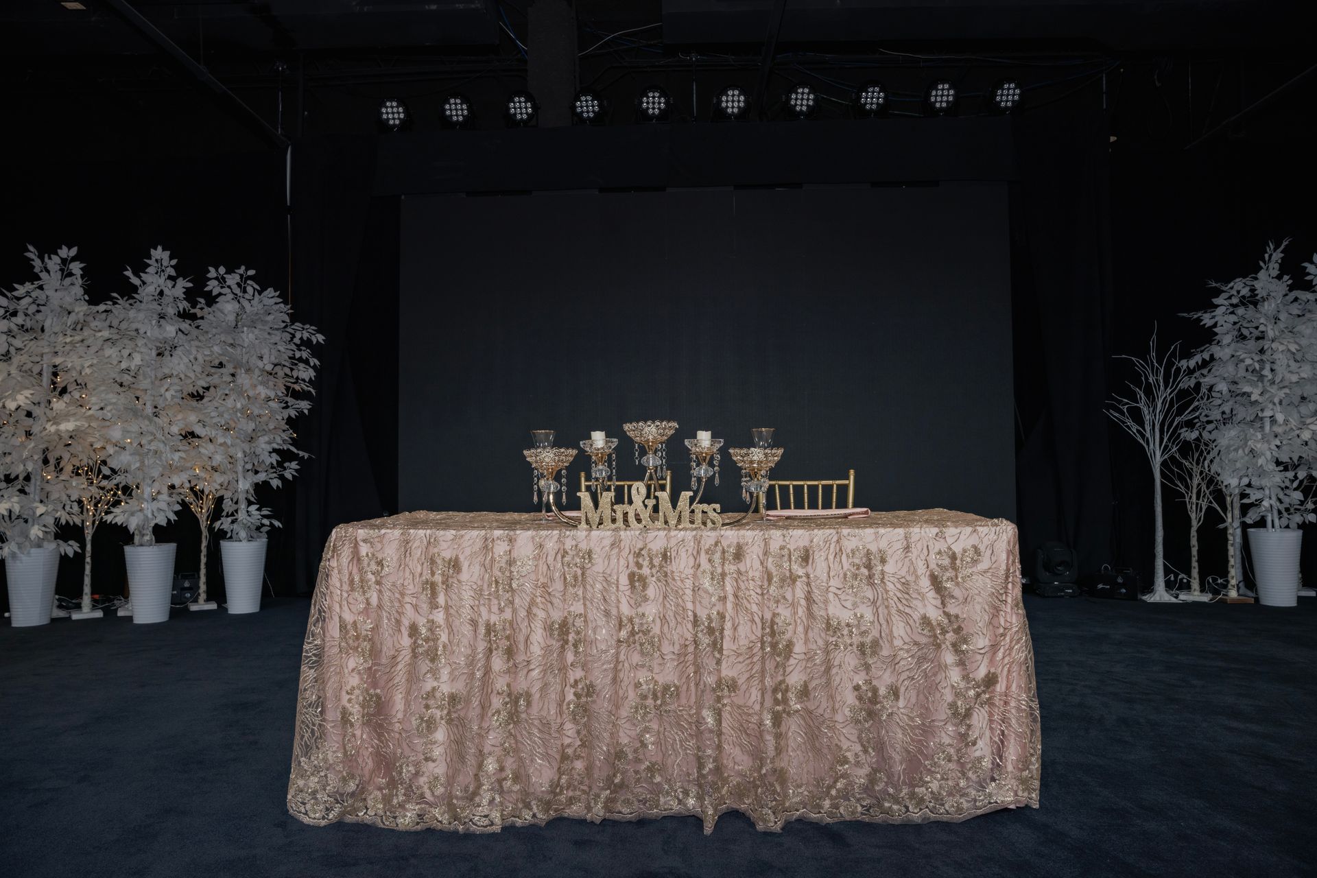 A table with a rose gold tablecloth sits in front of a stage.
