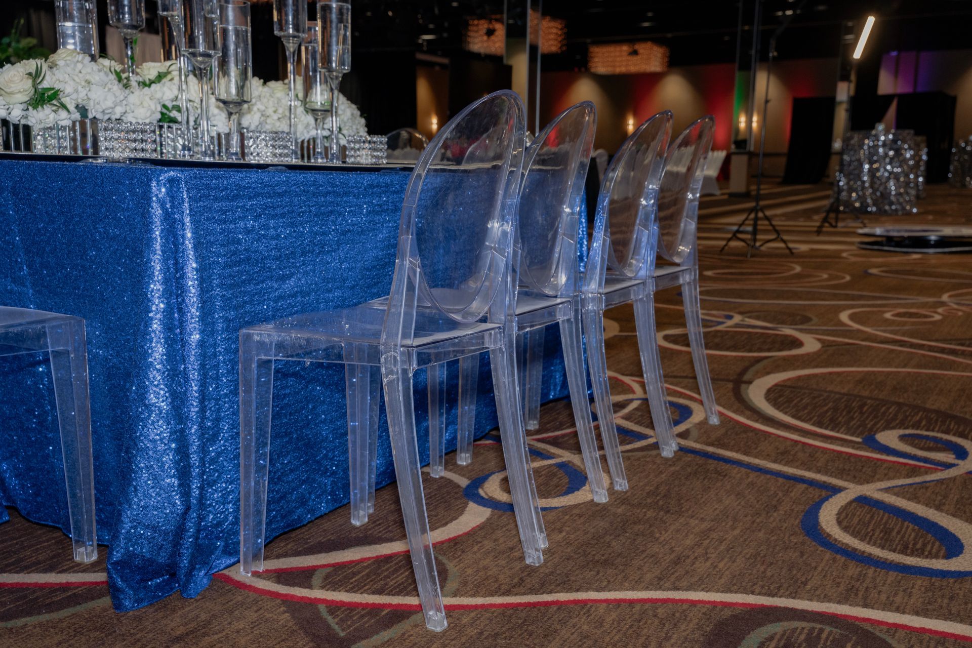 A row of clear chairs sitting next to a table with a blue table cloth.