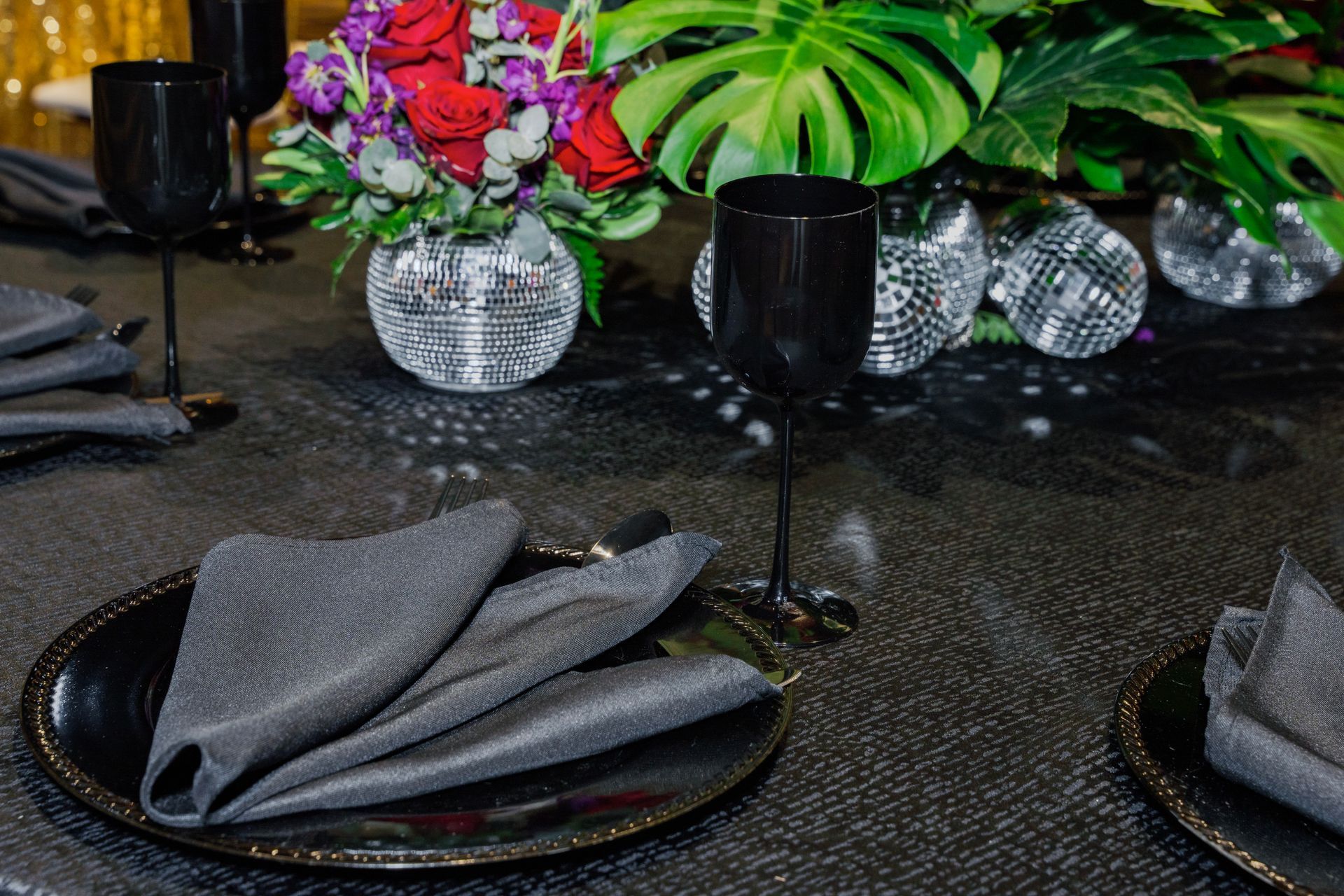 A table setting with plates , napkins , wine glasses and a vase of flowers.