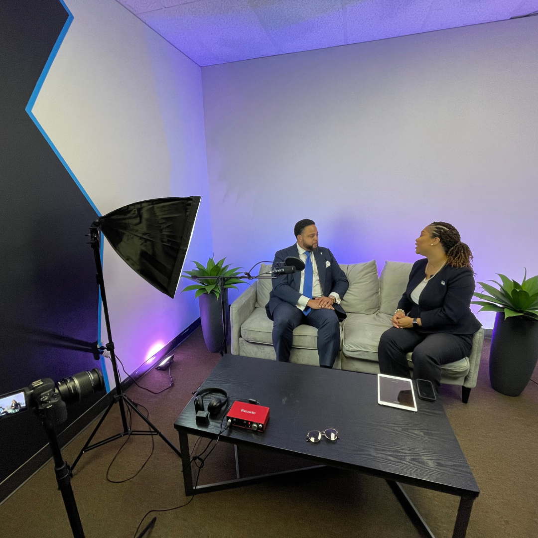 A man in a suit is sitting on a couch talking to a woman