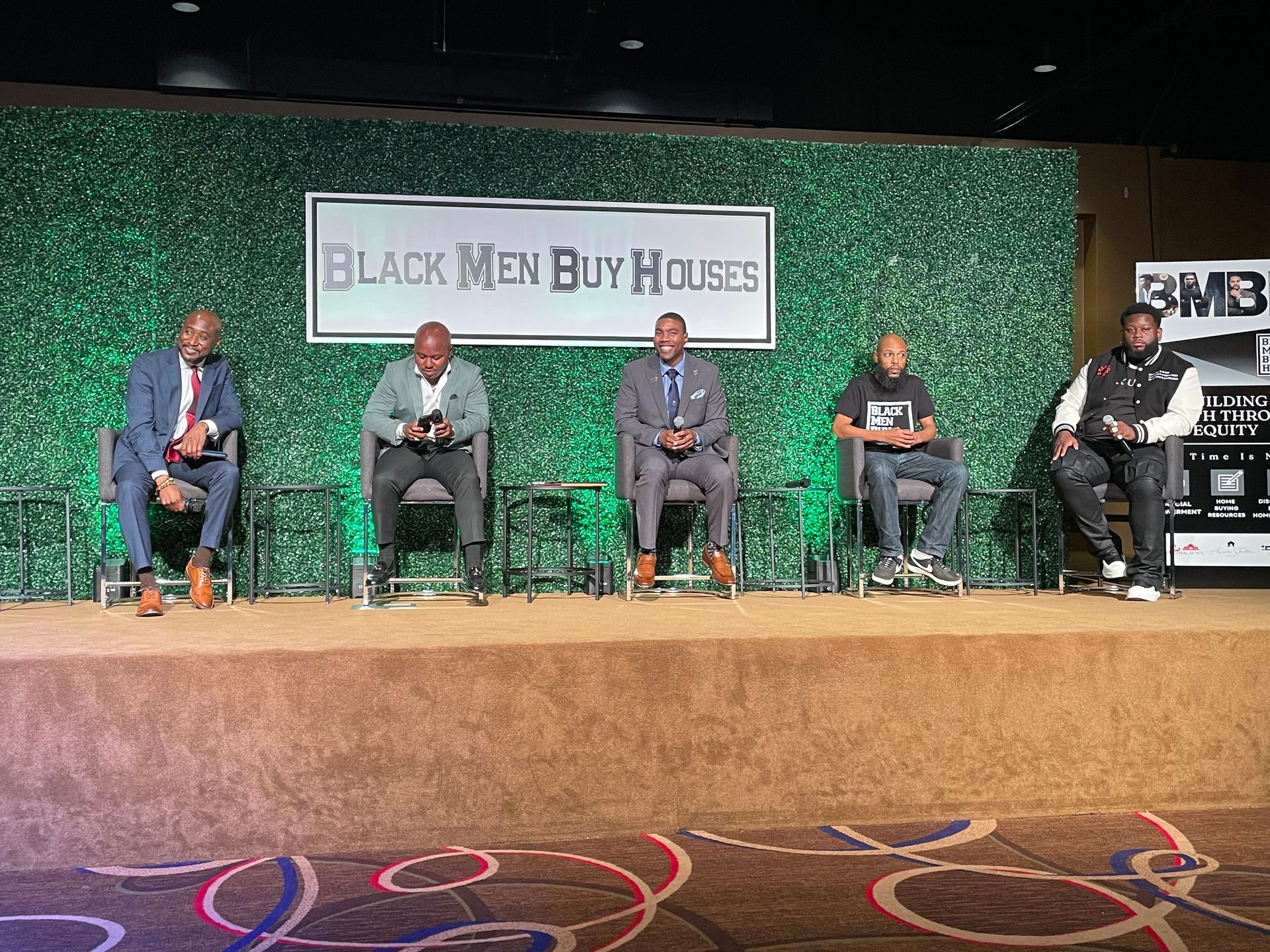 A group of men are sitting on a stage in front of a green wall.