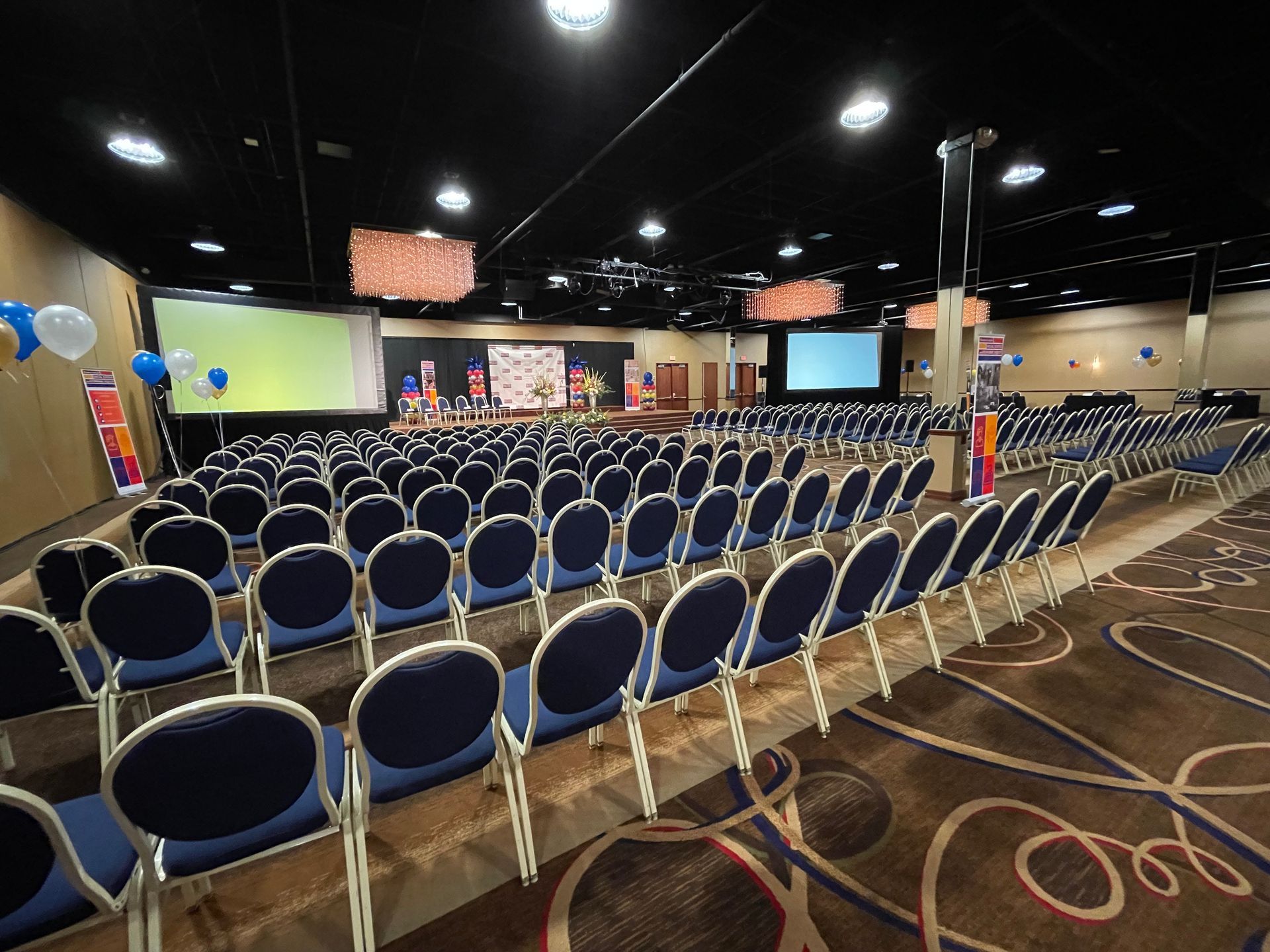 A large auditorium with rows of blue chairs and a large screen