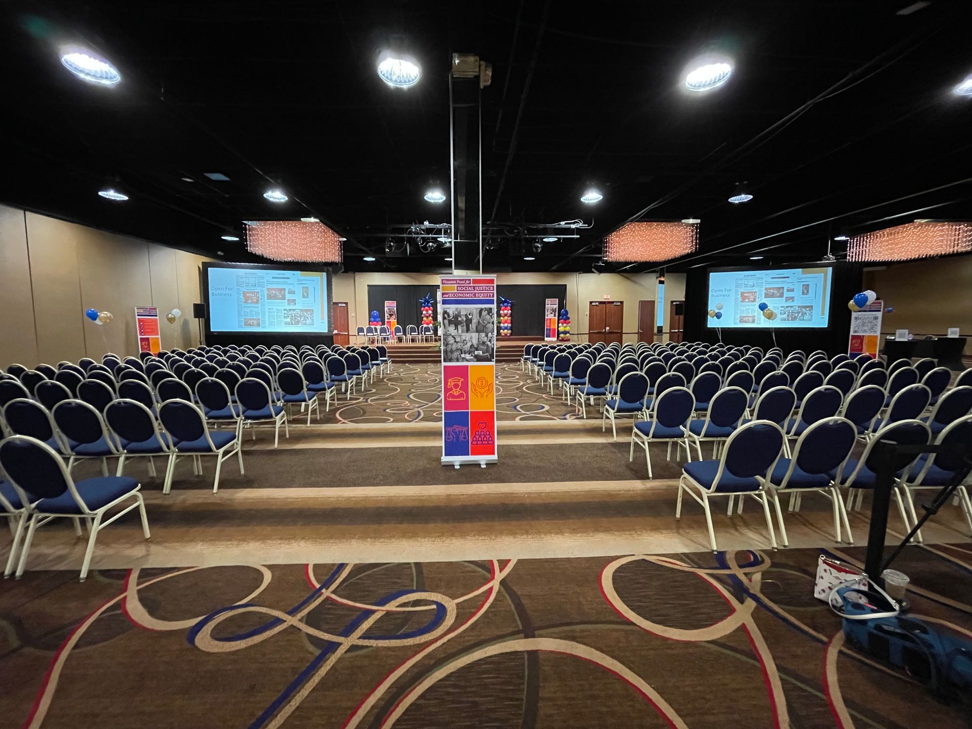 A large conference room with rows of chairs and projector screens.